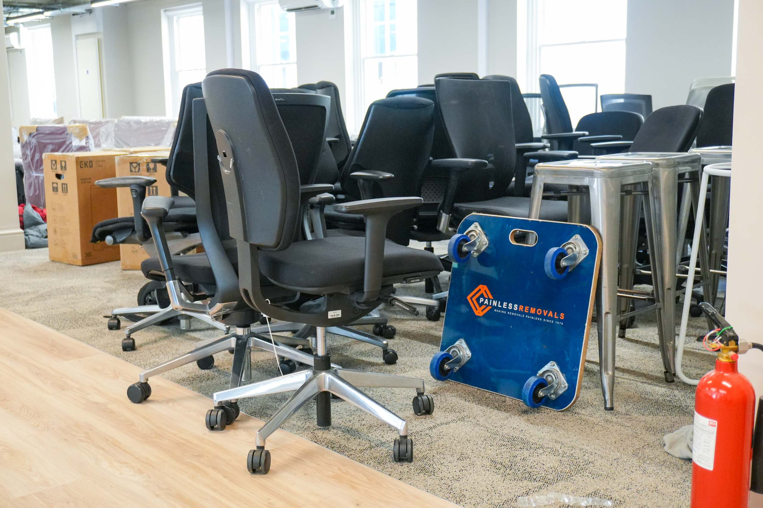 Painless Removals crew mid-relocation in a Bristol office — staged chairs and a branded moving skate